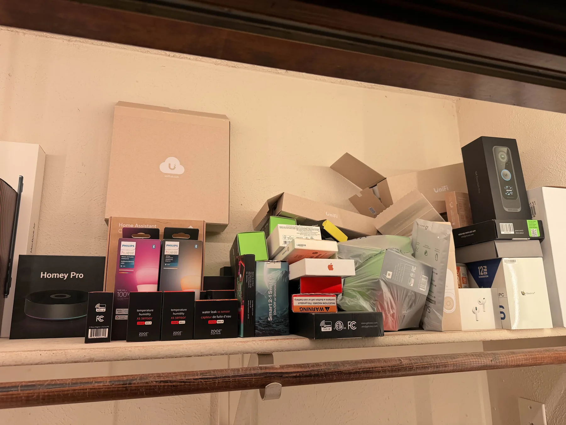 A shelf of smart home gear: Hue bulbs, Zooz Z-Wave sensors, UniFi, Homey Pro